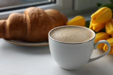Photo of Delicious morning coffee, croissant and flowers near window, closeup