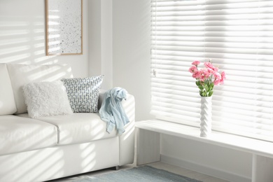 White vase with beautiful flowers near window in living room