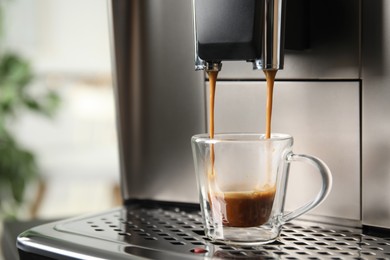 Espresso machine pouring coffee into glass cup against blurred background, closeup. Space for text