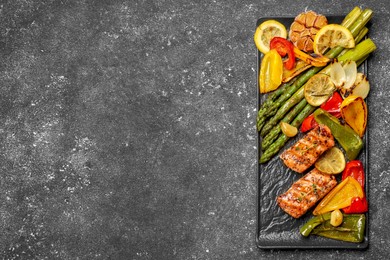 Photo of Tasty grilled salmon with lemon and vegetables on black table, top view. Space for text