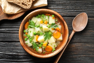 Bowl of fresh homemade vegetable soup served on dark wooden table, flat lay