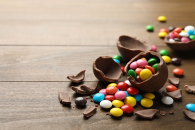 Photo of Broken chocolate eggs and colorful candies on wooden table. Space for text