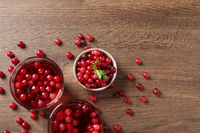 Photo of Tasty cranberry juice in glasses and fresh berries on wooden table, flat lay. Space for text