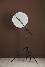 Photo of Studio reflector on tripod near brown wall indoors. Professional photographer's equipment