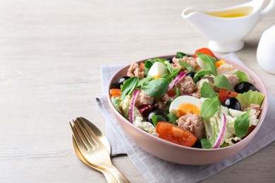 Photo of Bowl of delicious salad with canned tuna and vegetables served on white wooden table, space for text