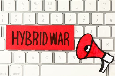 Photo of Card with words Hybrid War and paper megaphone on computer keyboard, top view