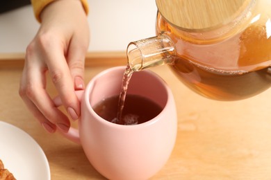 Photo of Woman pouring aromatic tea into cup at table, closeup