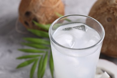 Photo of Glass of coconut water with ice cubes on grey table, closeup