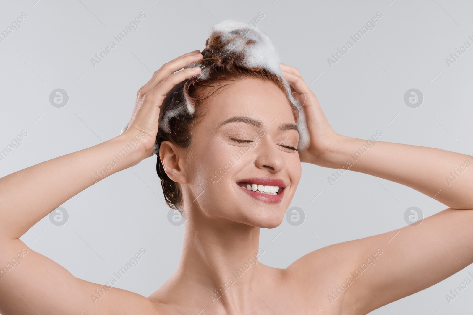 Photo of Happy young woman washing her hair with shampoo on light grey background