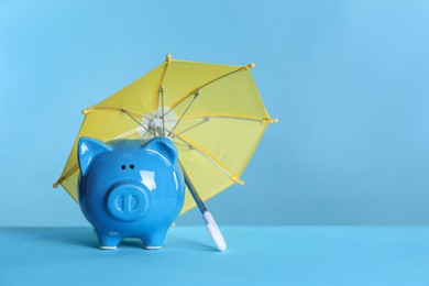 Photo of Small umbrella and piggy bank on light blue background. Space for text