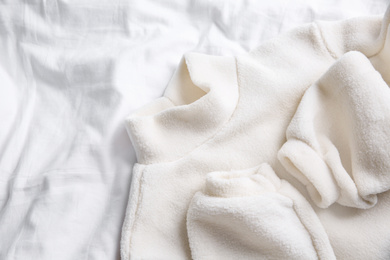 Warm fleece sweater on white crumpled fabric, top view