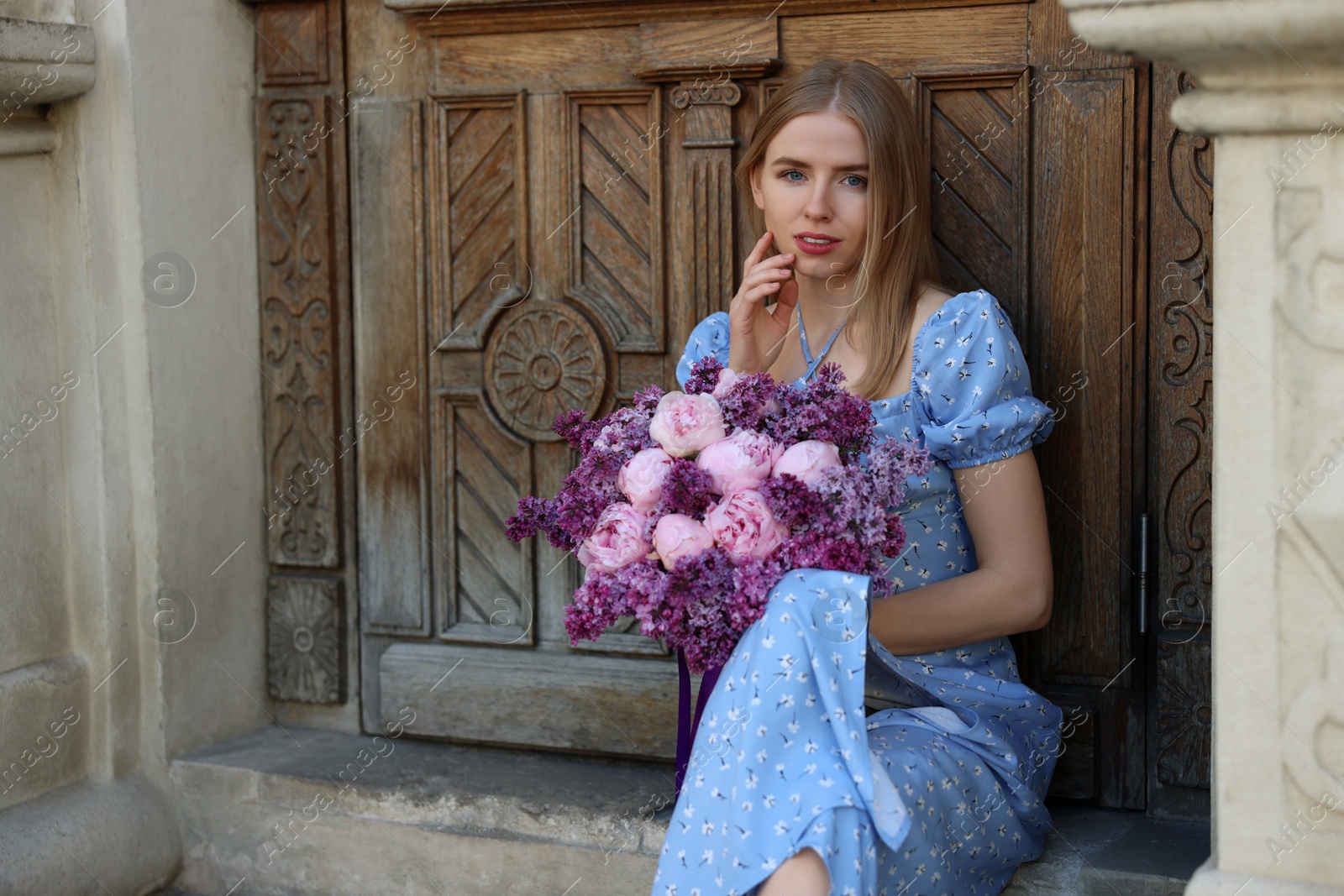 Photo of Beautiful woman with bouquet of spring flowers near building outdoors, space for text