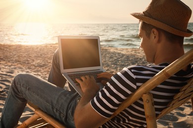 Photo of Man working with laptop in deck chair on beach