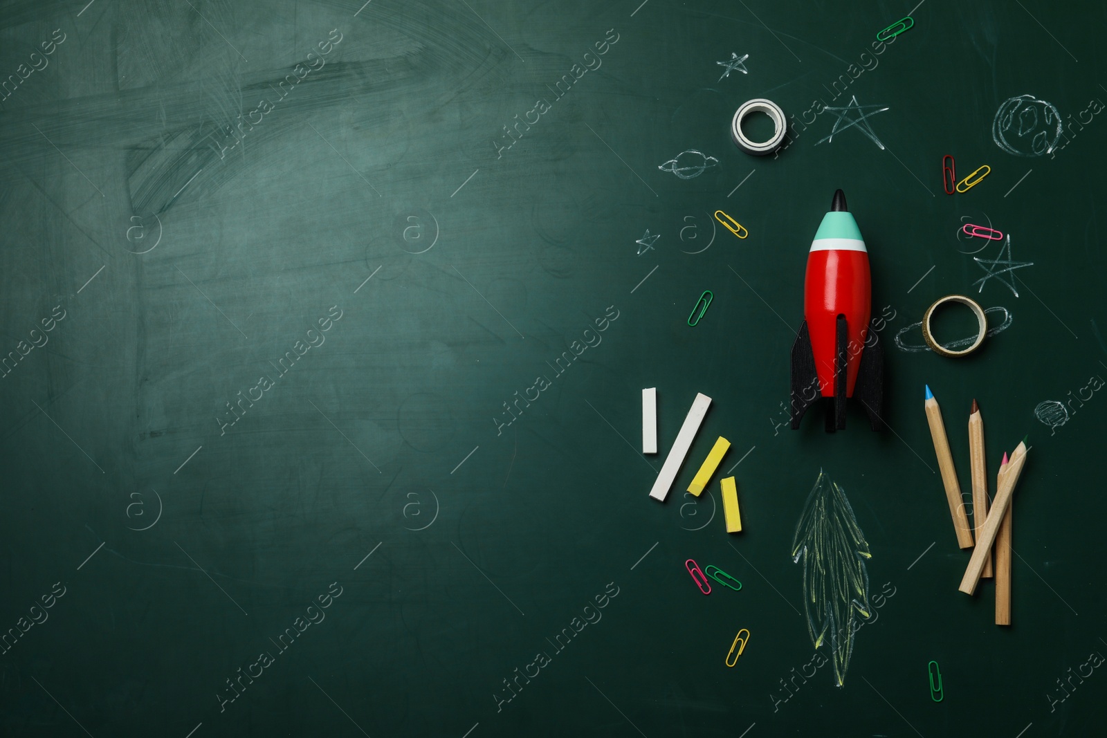 Photo of Bright toy rocket, school supplies and drawings on chalkboard, flat lay. Space for text