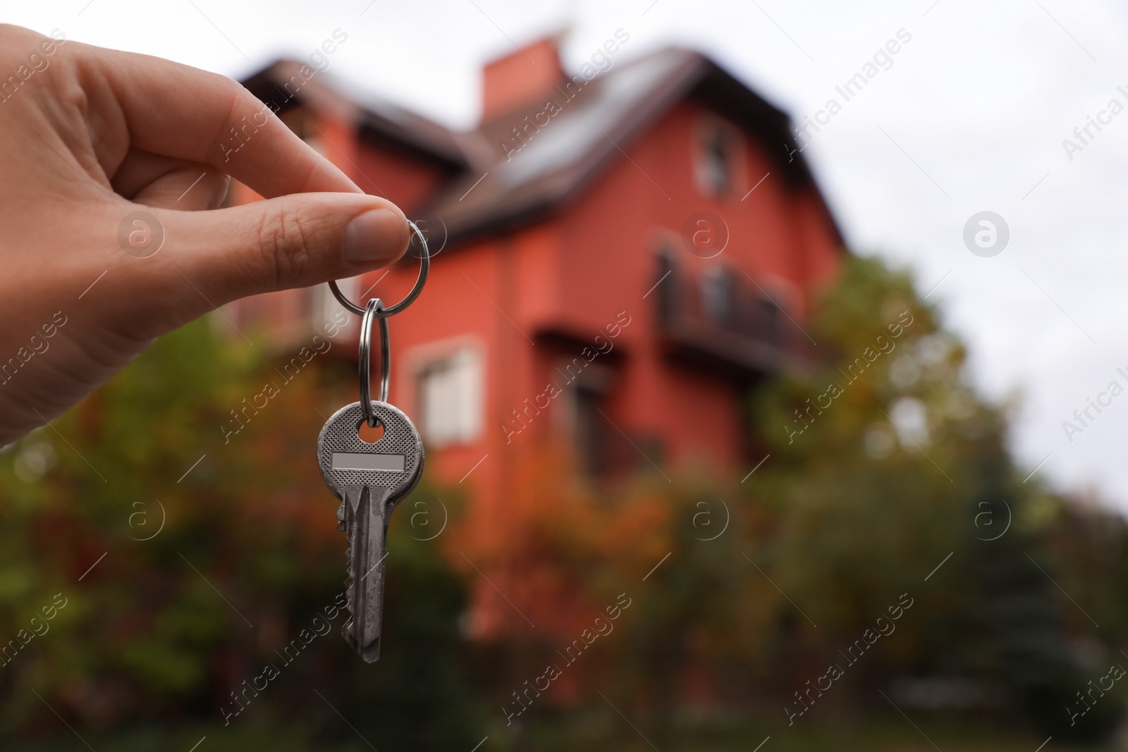 Photo of Real estate agent holding keys to new house outdoors, closeup. Space for text