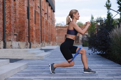 Photo of Fit woman doing exercise with fitness elastic band near building outdoors. Space for text