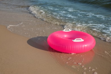 Bright pink inflatable ring on sandy beach near sea