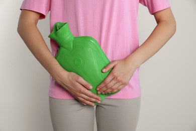 Photo of Woman using hot water bottle to relieve cystitis pain on light background, closeup