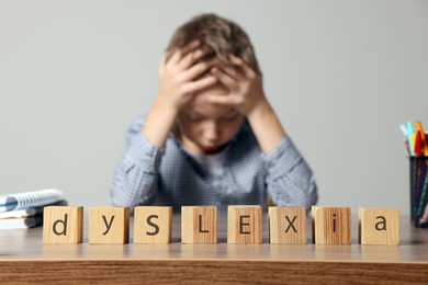 Little boy covering head with hands and cubes with word Dyslexia at wooden table, selective focus