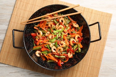 Shrimp stir fry with vegetables in wok and chopsticks on wooden table, top view