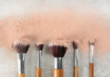 Makeup brushes and scattered face powder on grey stone table, flat lay