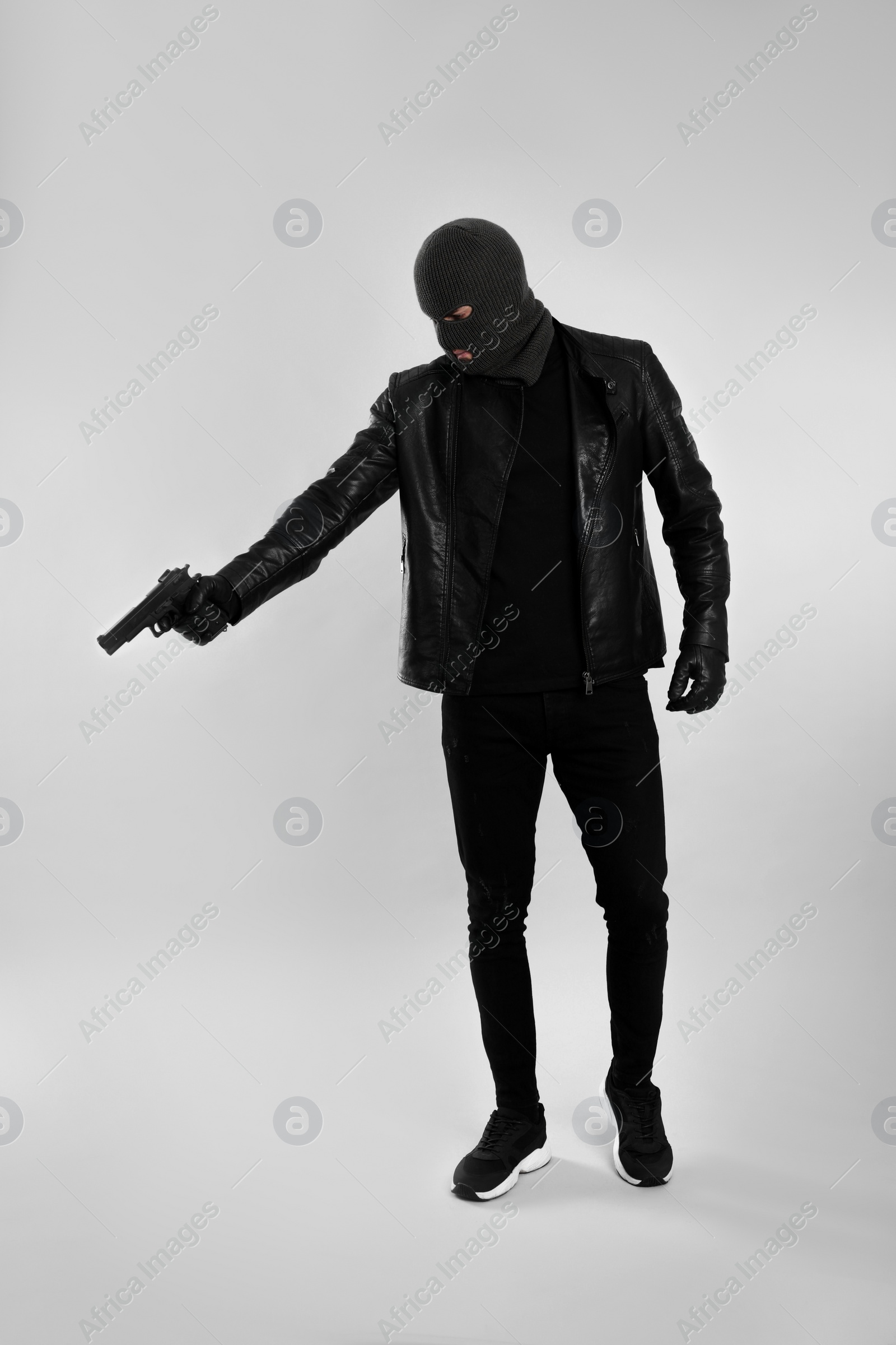 Photo of Man wearing knitted balaclava with gun on light grey background