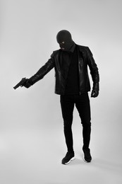 Man wearing knitted balaclava with gun on light grey background