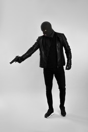 Photo of Man wearing knitted balaclava with gun on light grey background