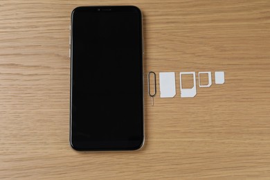 Photo of SIM cards, mobile phone and ejector tool on wooden table, flat lay
