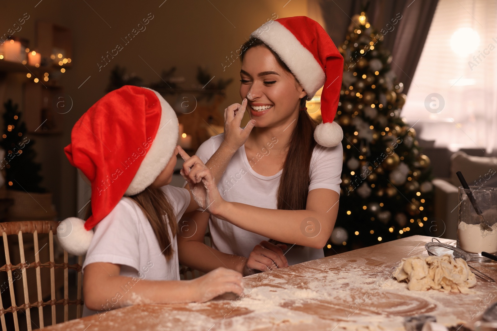 Photo of Mother with her cute little daughter having fun while making dough for Christmas cookies in kitchen