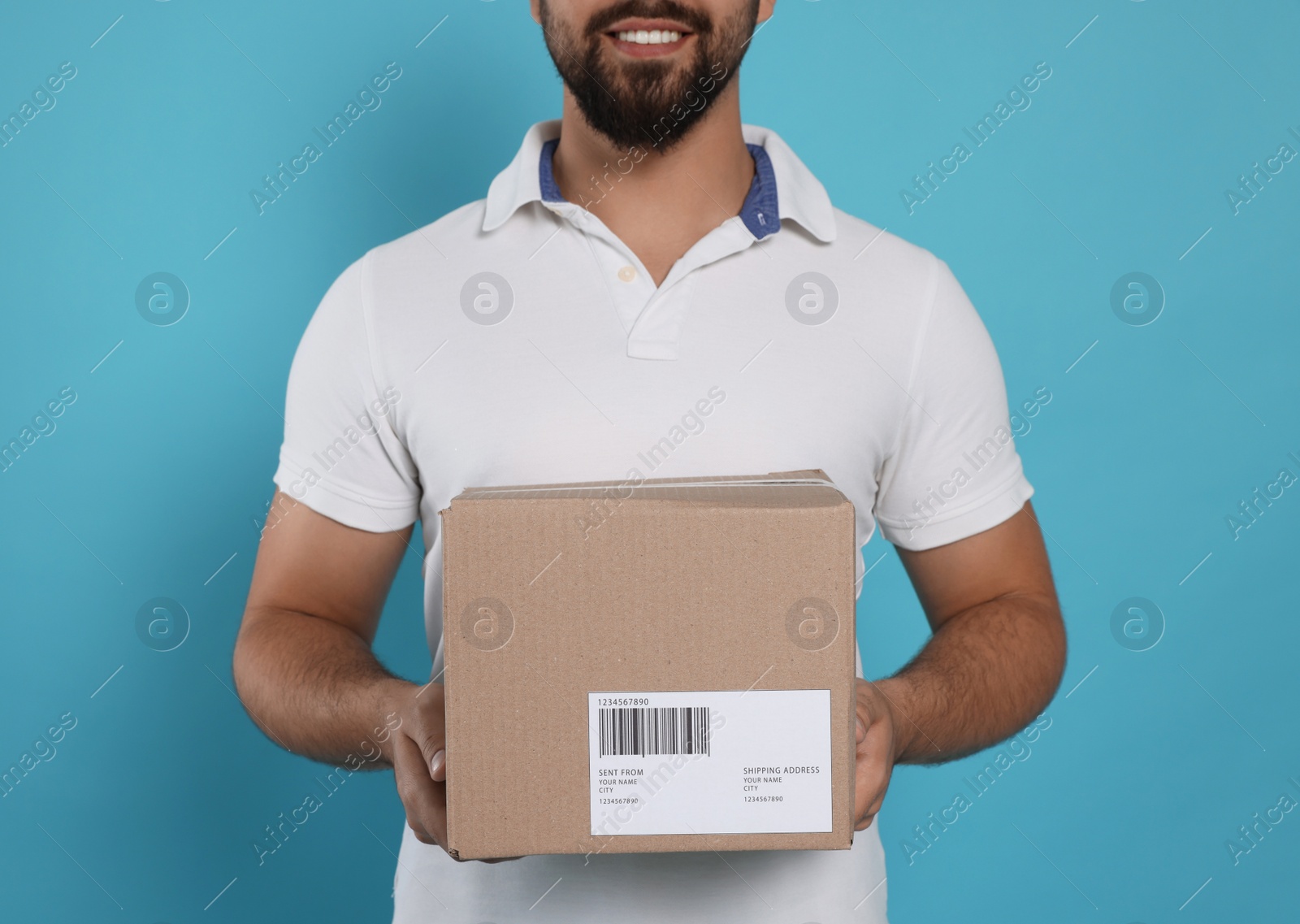Photo of Courier holding cardboard box on light blue background, closeup