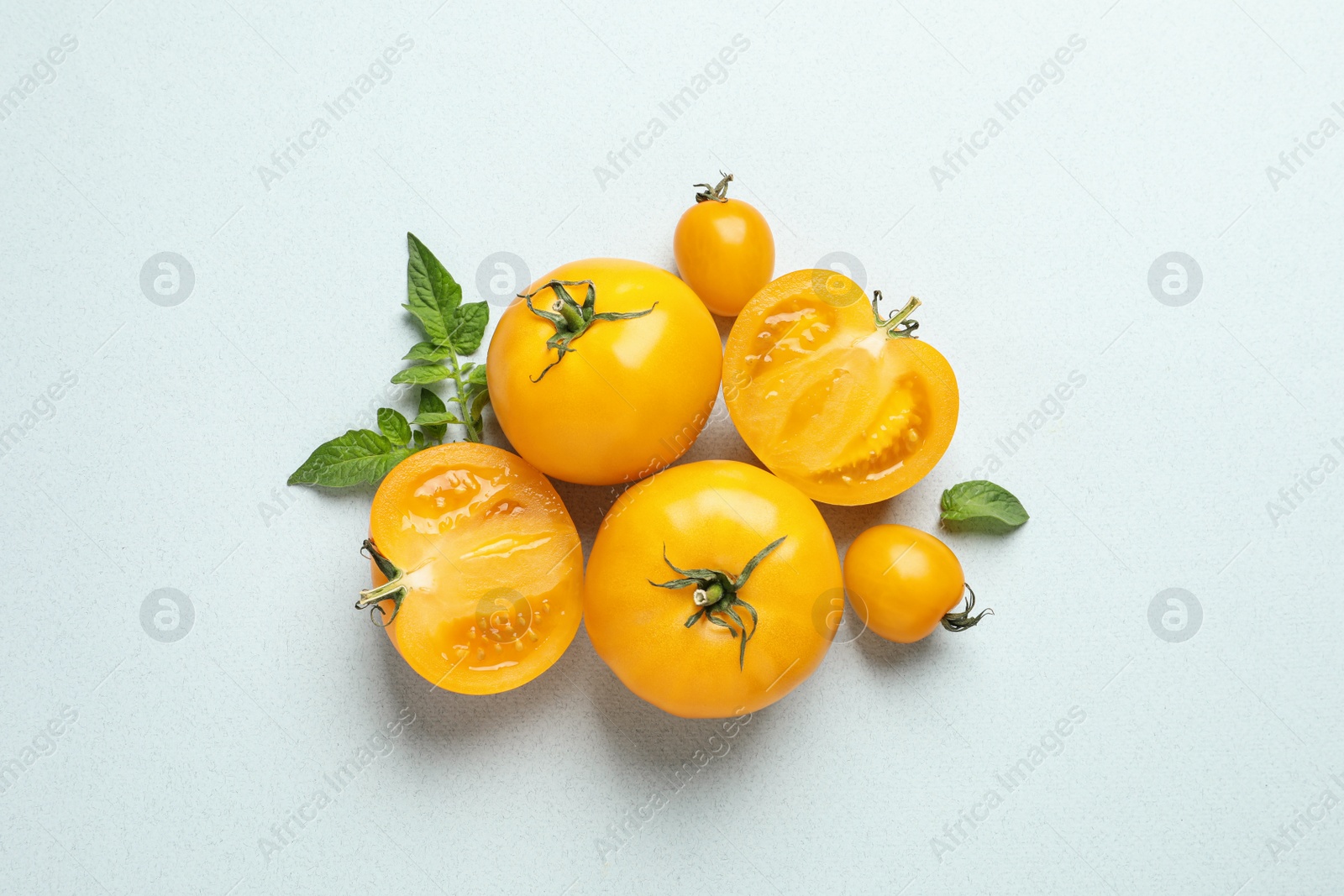 Photo of Cut and whole ripe yellow tomatoes with leaves on light background, flat lay