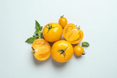 Photo of Cut and whole ripe yellow tomatoes with leaves on light background, flat lay