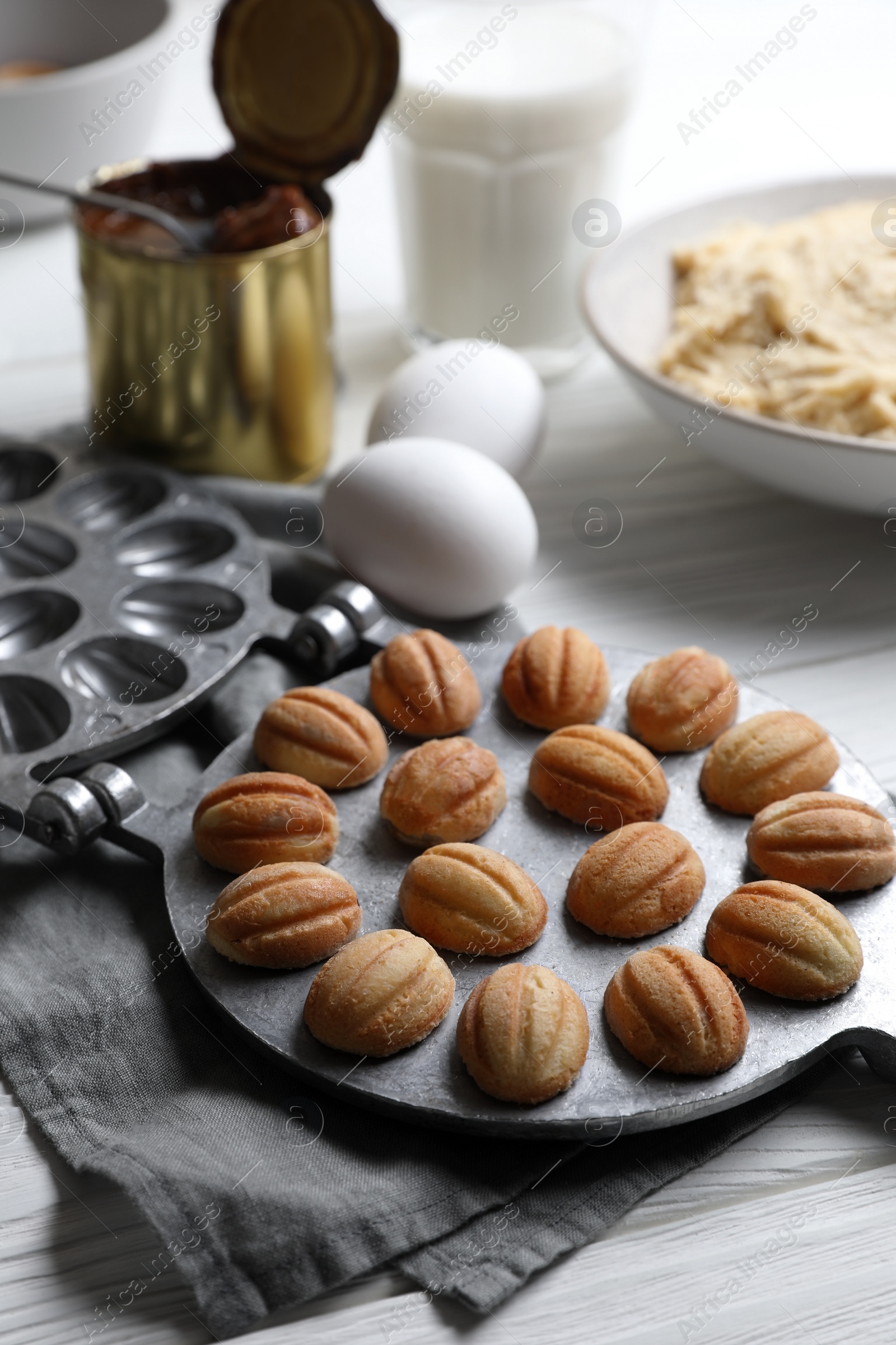 Photo of Delicious walnut shaped cookies with condensed milk and ingredients on white wooden table, closeup