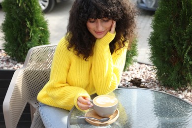 Photo of Young woman in stylish yellow sweater with cup of coffee at table outdoors