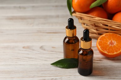 Photo of Bottles of tangerine essential oil on white wooden table, space for text