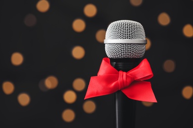 Microphone with red bow against blurred lights, space for text. Christmas music