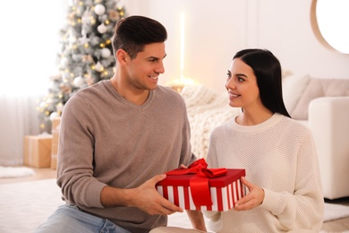 Photo of Couple holding gift box in room with Christmas tree