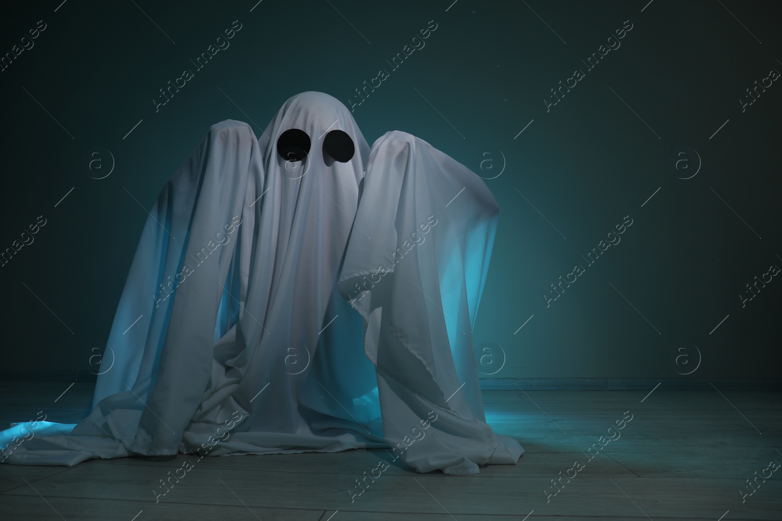 Photo of Creepy ghost. Woman covered with sheet on dark teal background