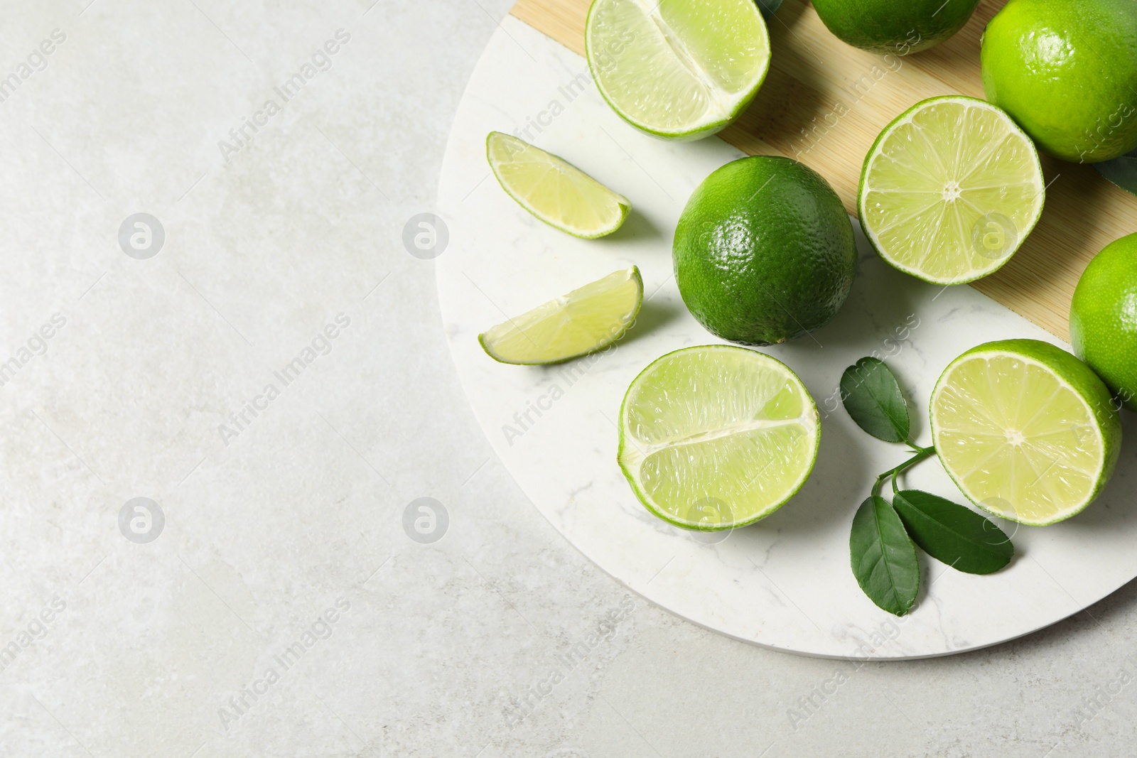 Photo of Fresh ripe limes and leaves on light table, top view. Space for text