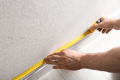 Photo of Man measuring baseboard indoors, closeup. Construction tool