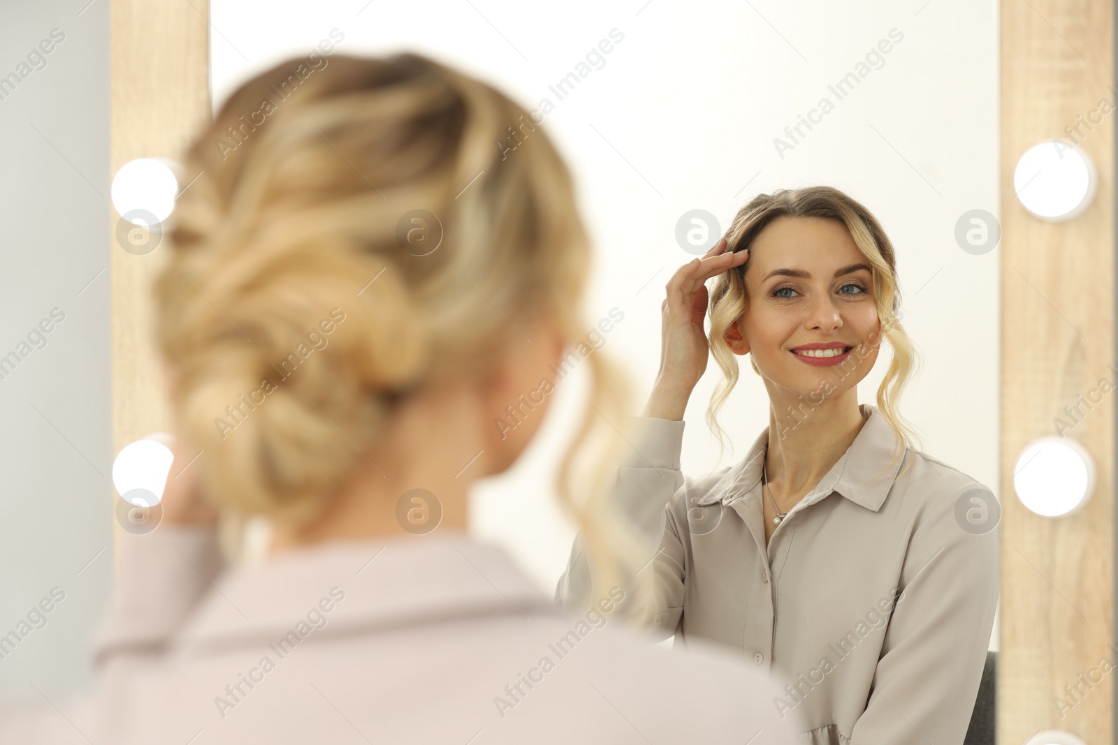 Photo of Smiling woman with beautiful hair style looking at mirror indoors