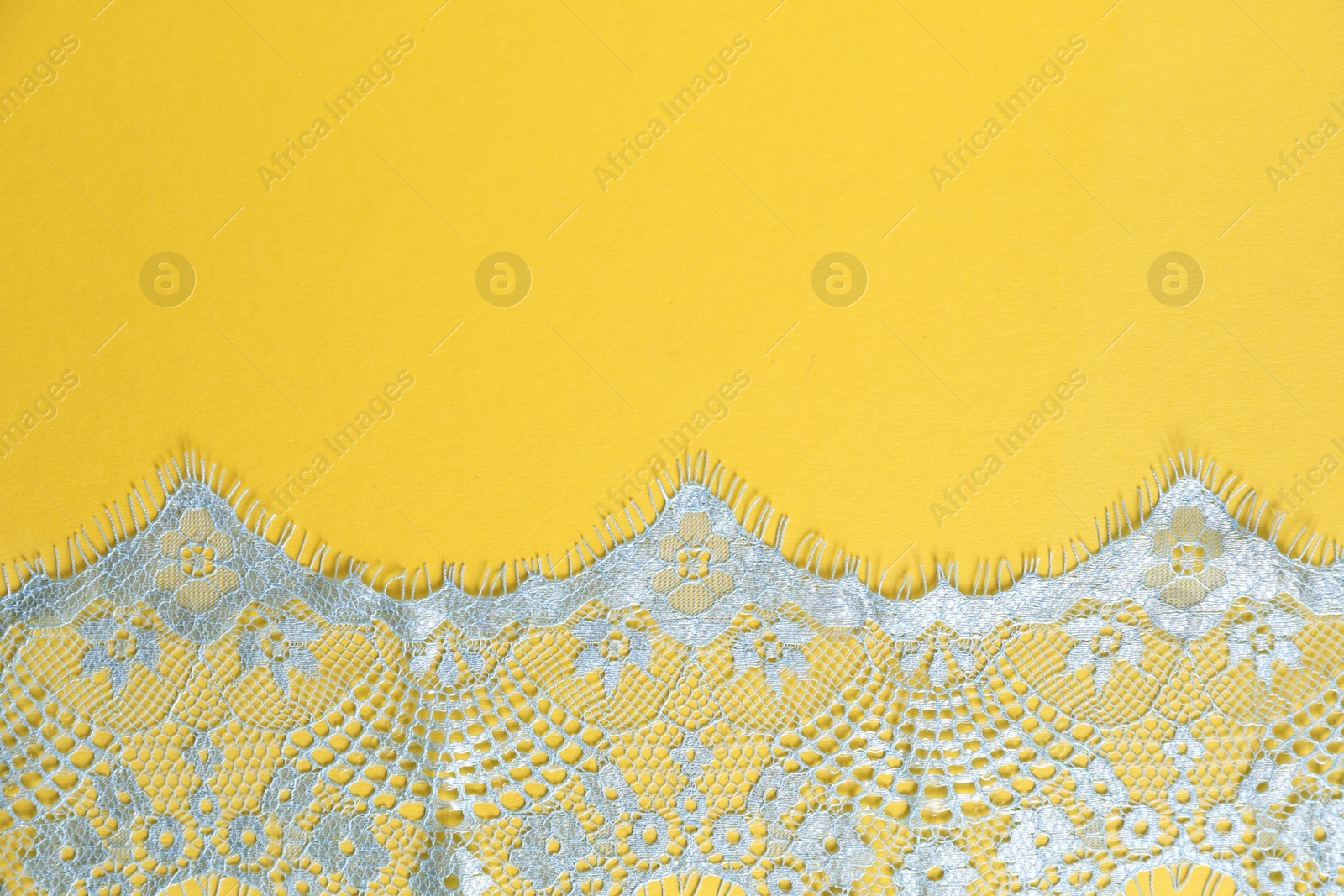 Photo of Light blue lace on yellow background, top view. Space for text