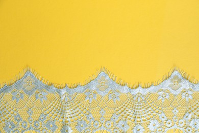 Photo of Light blue lace on yellow background, top view. Space for text