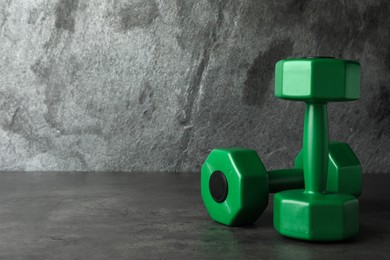 Photo of Green vinyl dumbbells on table against grey background. Space for text