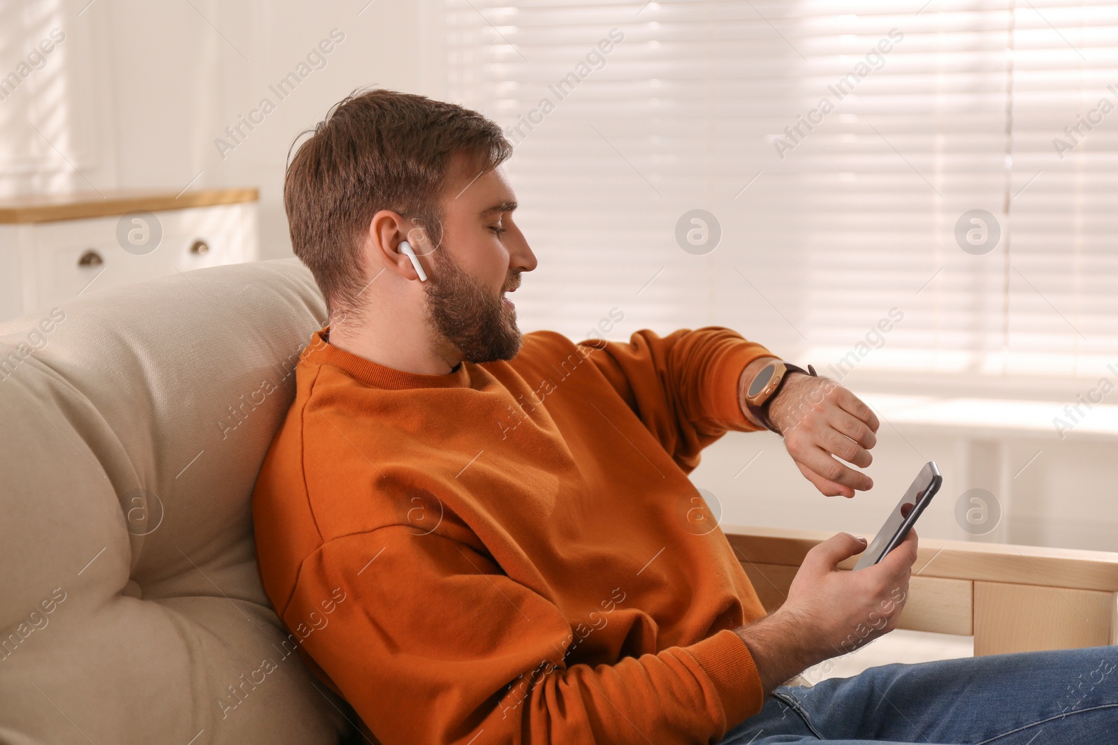 Photo of Young man with smart watch, phone and earphones at home