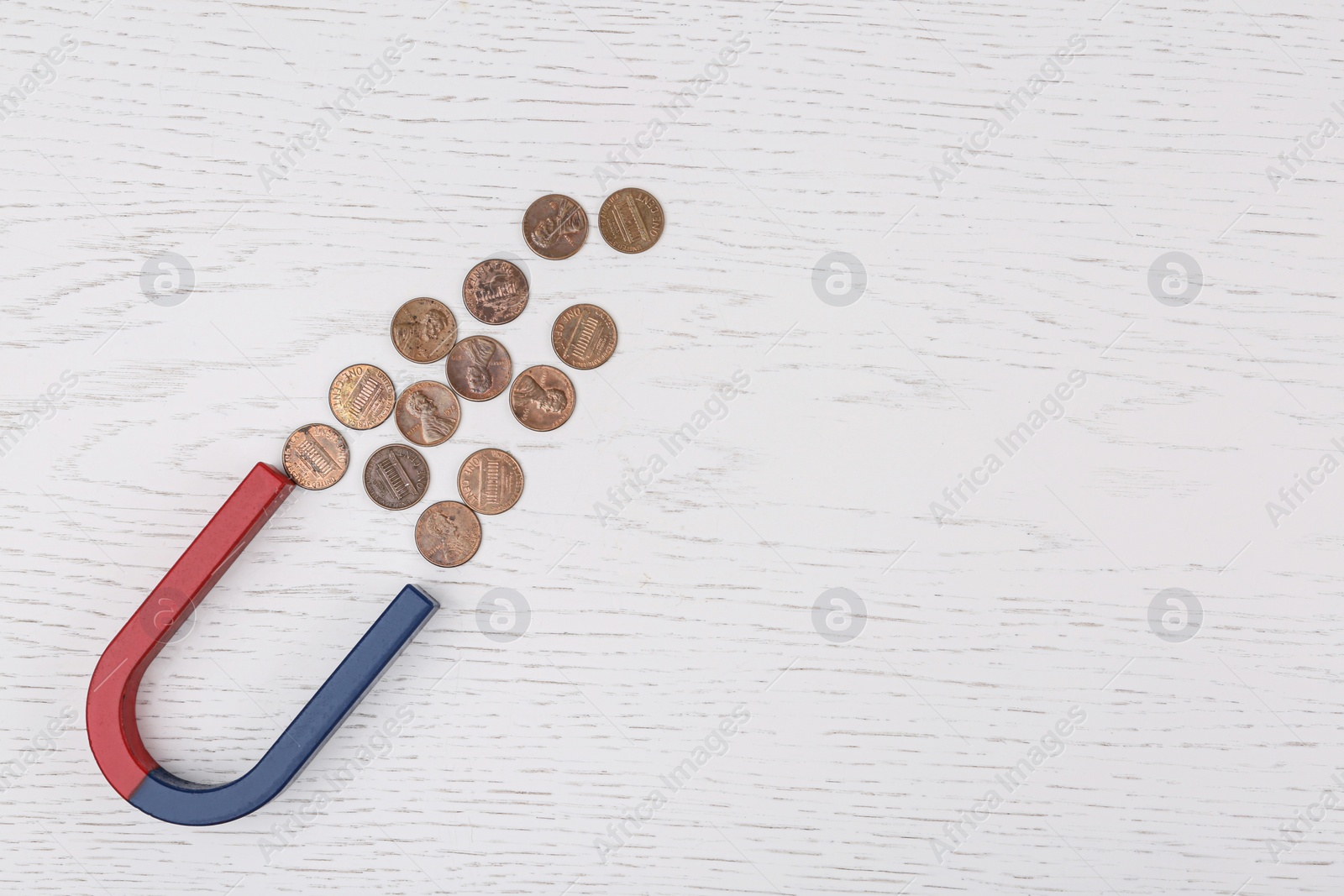 Photo of Magnet attracting coins on white wooden table, flat lay. Space for text