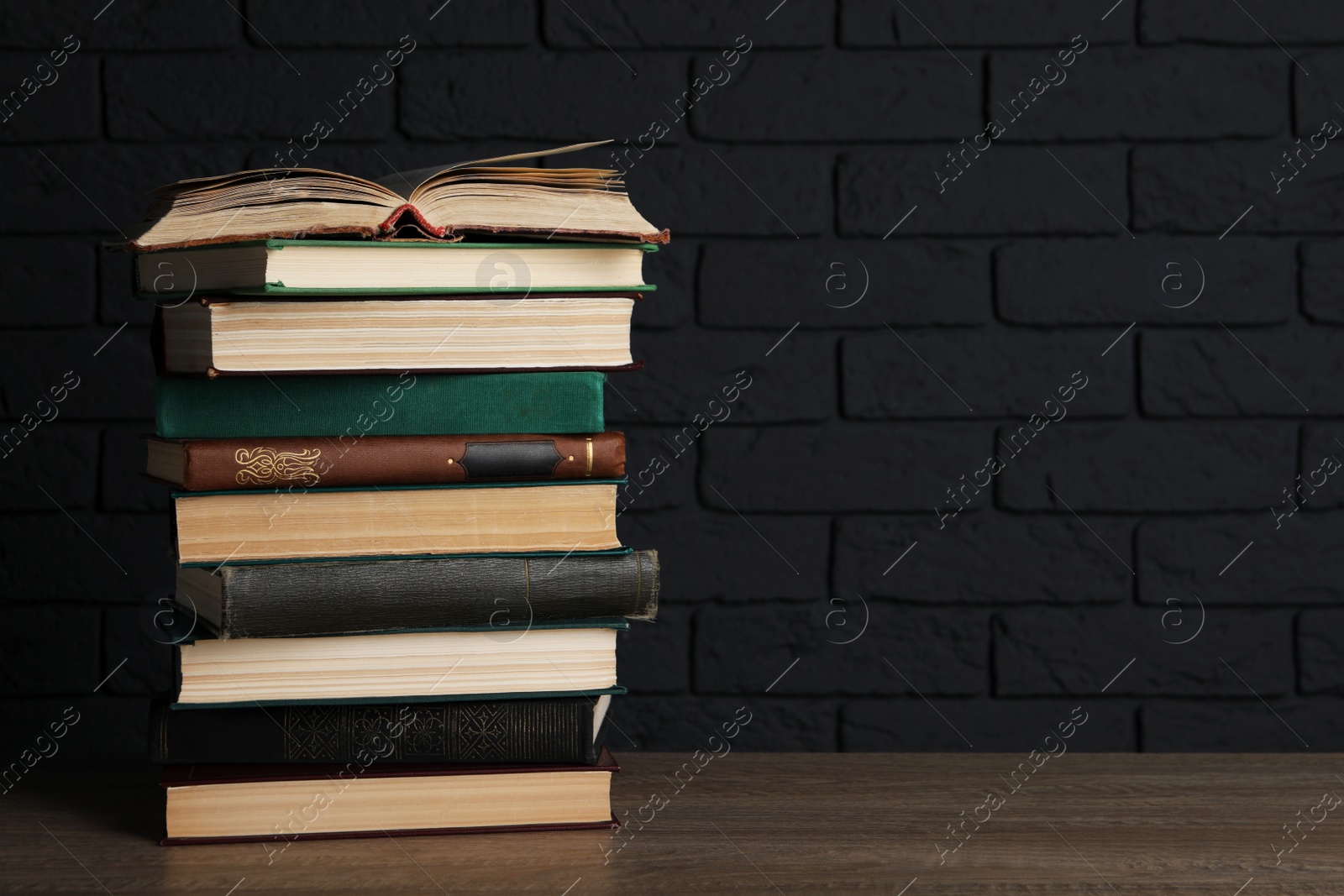 Photo of Stack of old hardcover books on wooden table near black brick wall, space for text