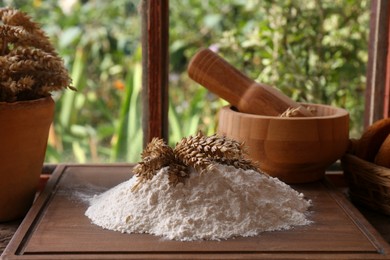 Photo of Pile of wheat flour and spikes on wooden board indoors