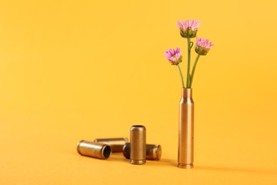 Photo of Bullet cartridge cases and beautiful chrysanthemum flowers on yellow background, space for text
